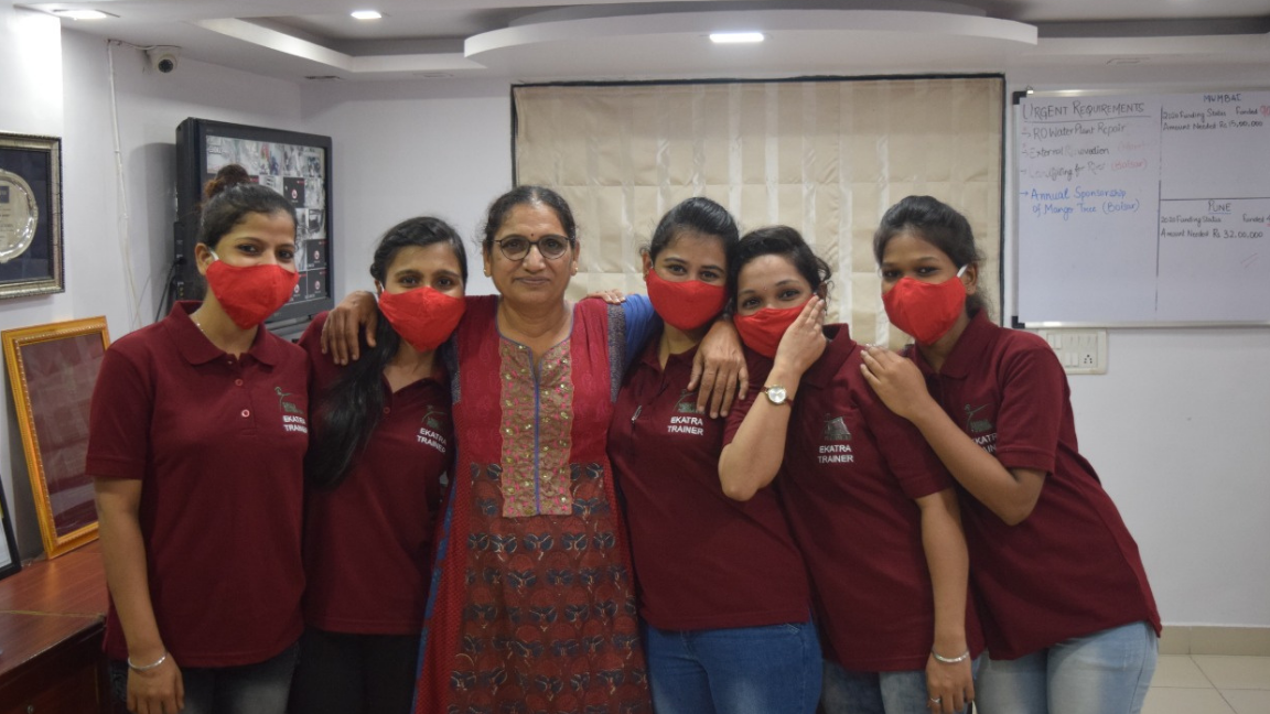 Five young women in Ekatra trainer polo shirts standing with a Rescue Foundation staff member in front of a planning board.