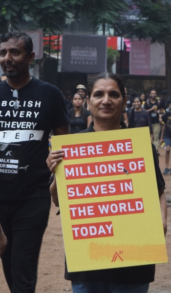 A woman marching in Mumbai holding a yellow placard reading 'There are millions of slaves in the world today', beside a man in an 'Abolish slavery' shirt.